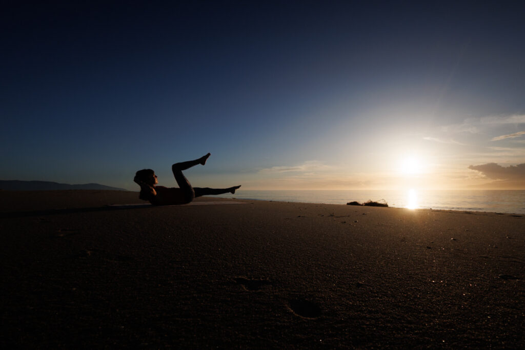 Personal Trainerin am Strand zum Sonnenuntergang beim Bauchtraining