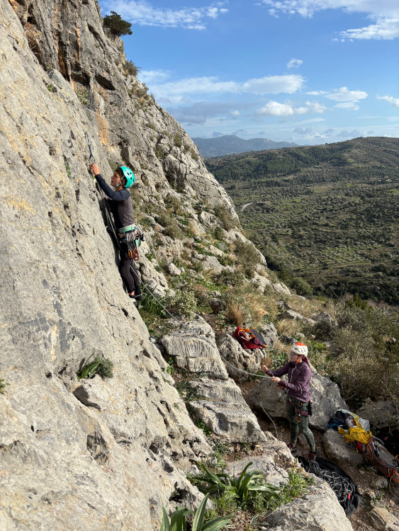 Kletterin am Fels ist gerade dabei den ersten Haken zu Clippen und Sichernde ist konzentriert dabei