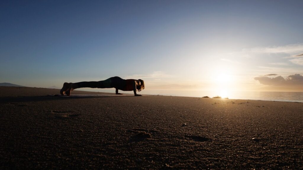 Personal Trainerin macht tiefen Liegestütz zum Sonnenuntergang am Strand