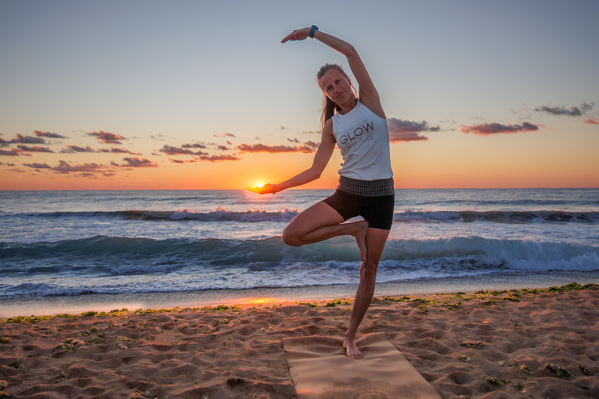 Yogalehrer vorm dem Meer am Strand zum Sonnenuntergang hält Sonnenball optisch in der Hand